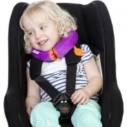 Mała dziewczynka w foteliku samochodowym ma na szyi zagłówek od marki Trunki.