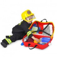 Chłopiec w stroju strażaka pakuje swoje skarby do walizki firmy Trunki.