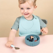 Dziecko siedzące przy stole spożywa posiłek z talerzyka silikonowego w niebieskim kolorze.