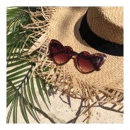 Przeciwsłoneczne okulary w kształcie serca leżą na plaży wraz z kapeluszem.