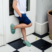 Chłopiec oparty o ścianę ma na sobie wygodne, miętowe buty.