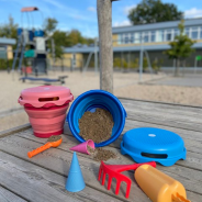 Piaskownica, w której znajdują się kolorowe zabawki do piasku.