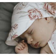 Śpiące niemowlę ma na główce chusteczkę z wiskozy bambusowej w kwiaty.