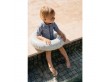 Mały chłopiec siedzący na brzegu basenu ma na sobie koło do pływania w niebieskim, pastelowym kolorze.