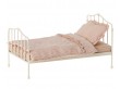 Metalowe łóżko dla lalek z różową pościelą.