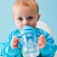 Mały chłopiec pije wodę z niebieskiego kubka ze słomką.