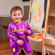 Chłopiec malujący farbami ma na sobie ochronny fartuszek w kolorze fioletowym.