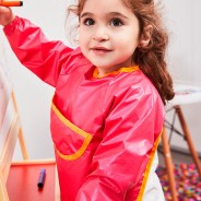 Kilkuletnia dziewczynka ubrana w fartuszek w różowym kolorze maluje farbami.